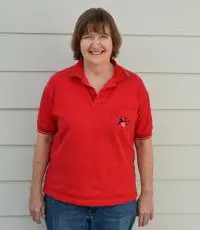 A woman in red shirt standing next to white wall.