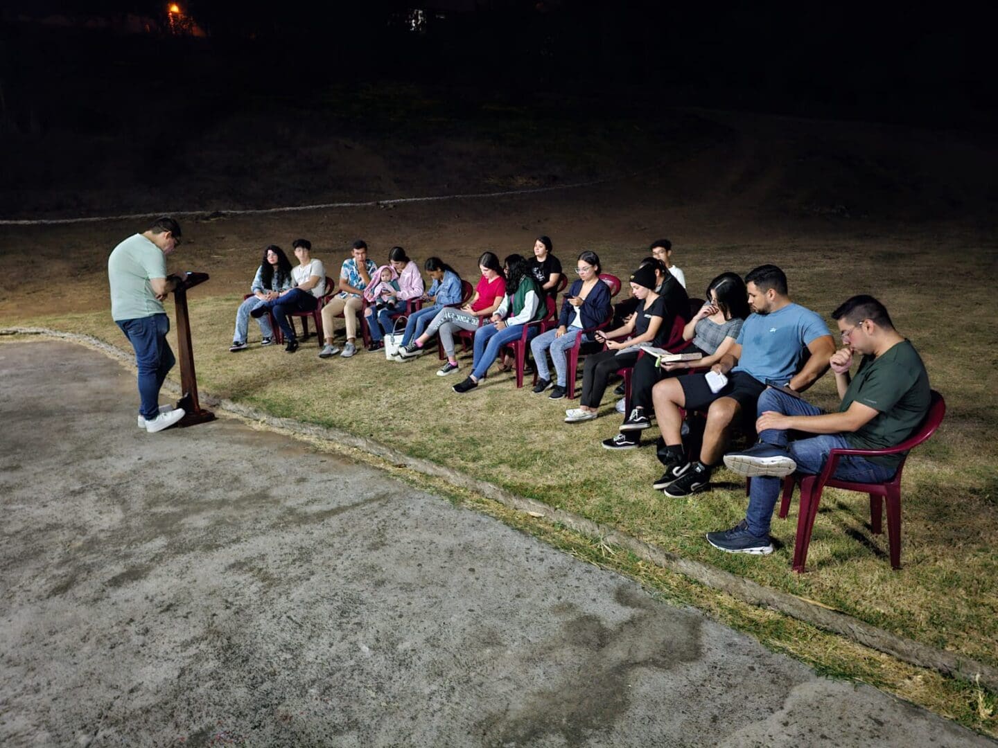 A group of people sitting on the ground in front of a man.