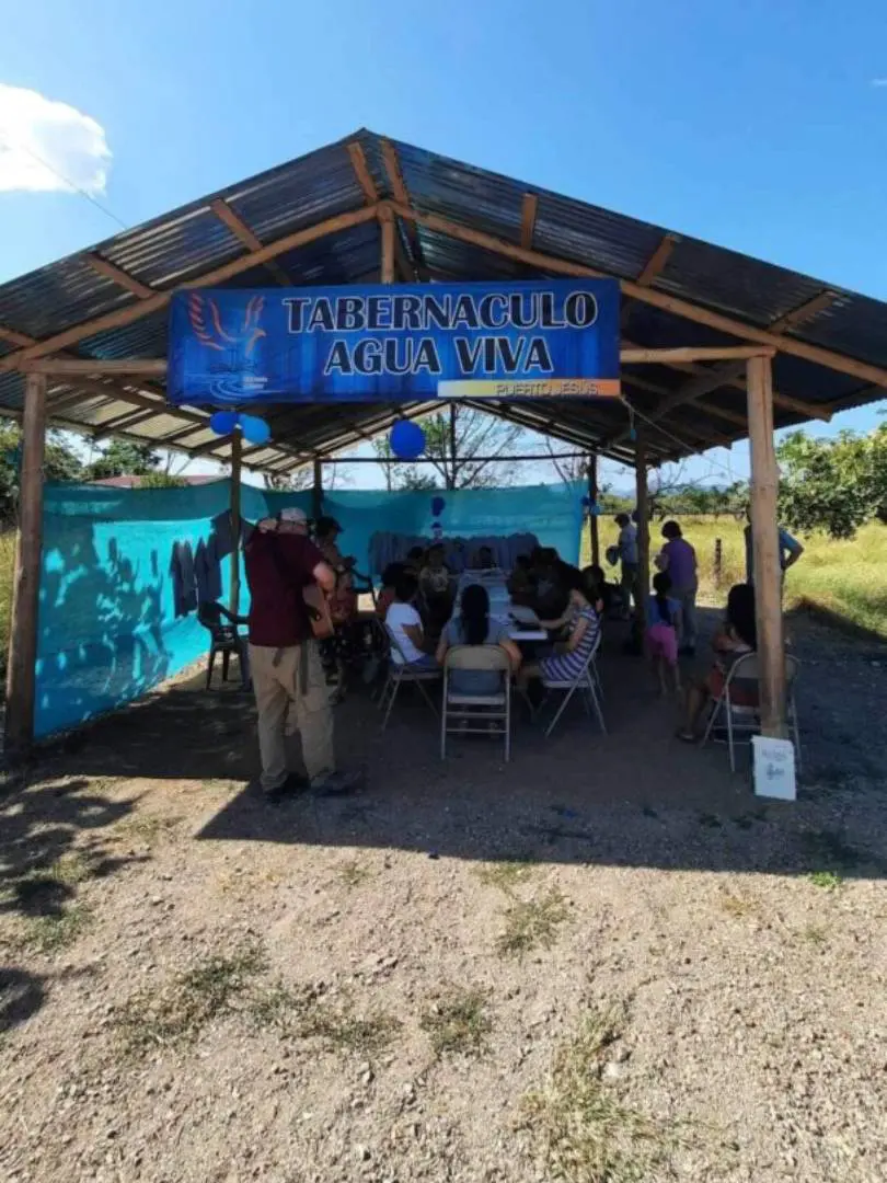 A group of people sitting at tables under a blue tent.